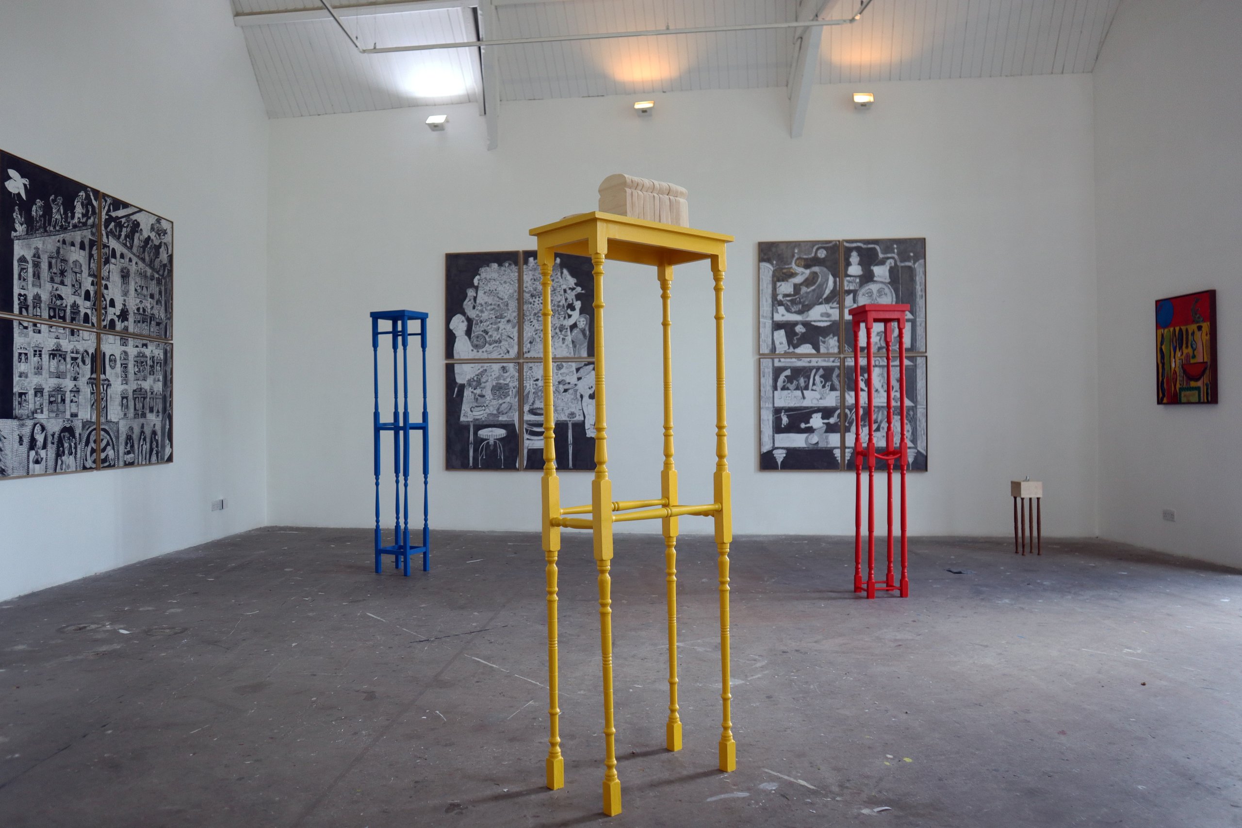Rufus Newell; Tall Tables at Patrick Studios. Three sculptural forms, yellow blue and red alike side tables but with extended legs stand in a large space with other works on the walls surrounding
